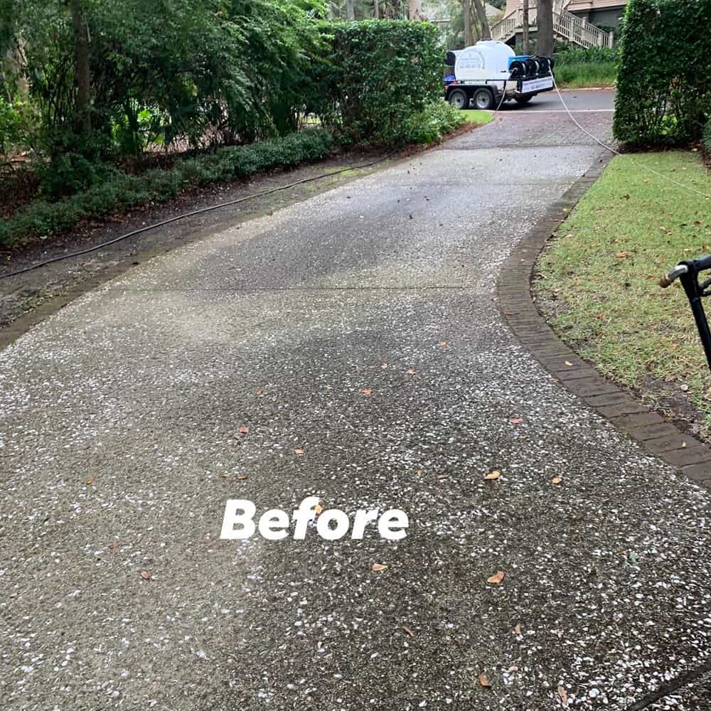 Pepper's Pressure Washing surface cleaner mid-pass on a Charleston concrete driveway, revealing the dramatically cleaned strip against the dirty surrounding concrete